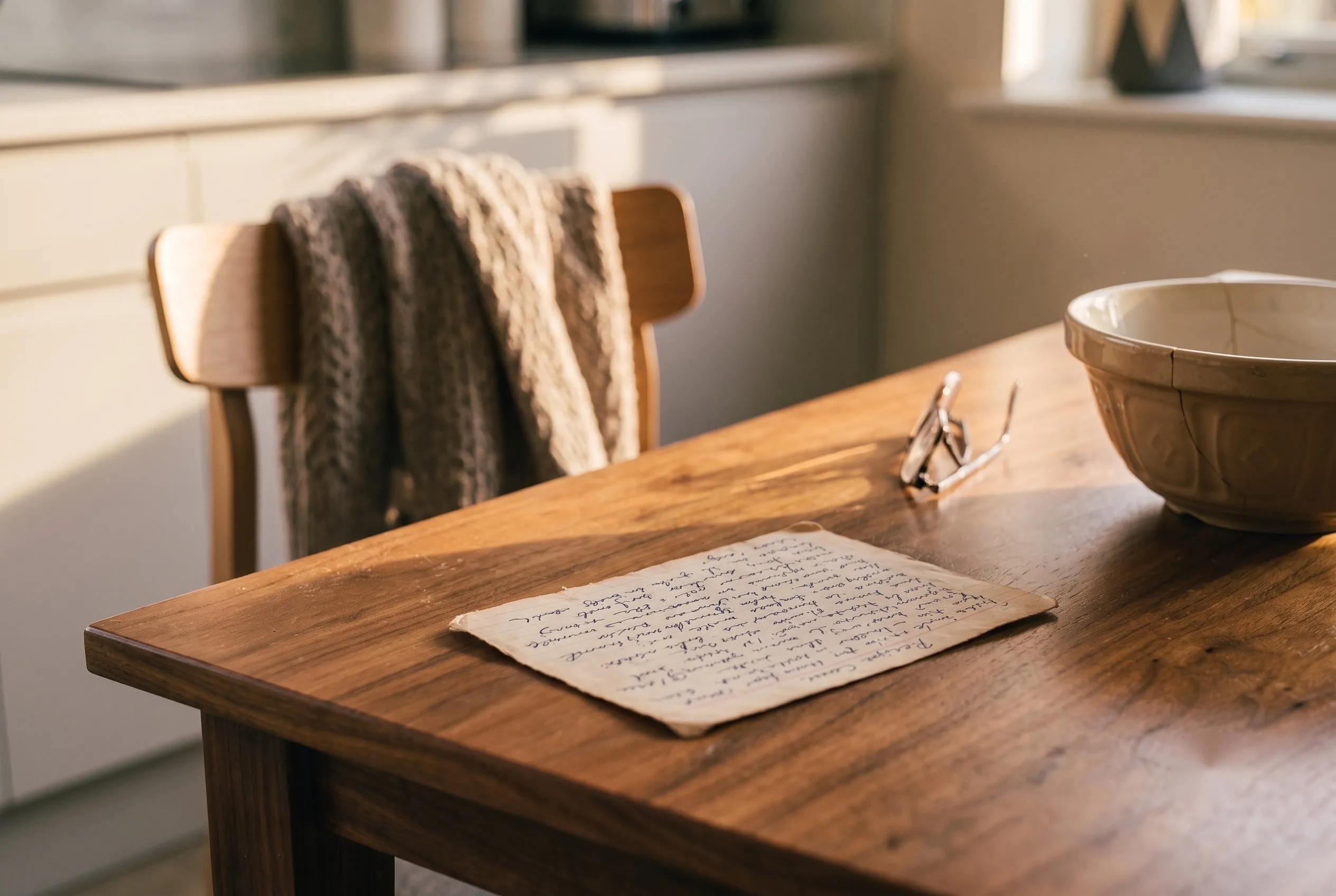 A recipe card covered in handwriting on a kitchen table, an empty chair pushed back behind it