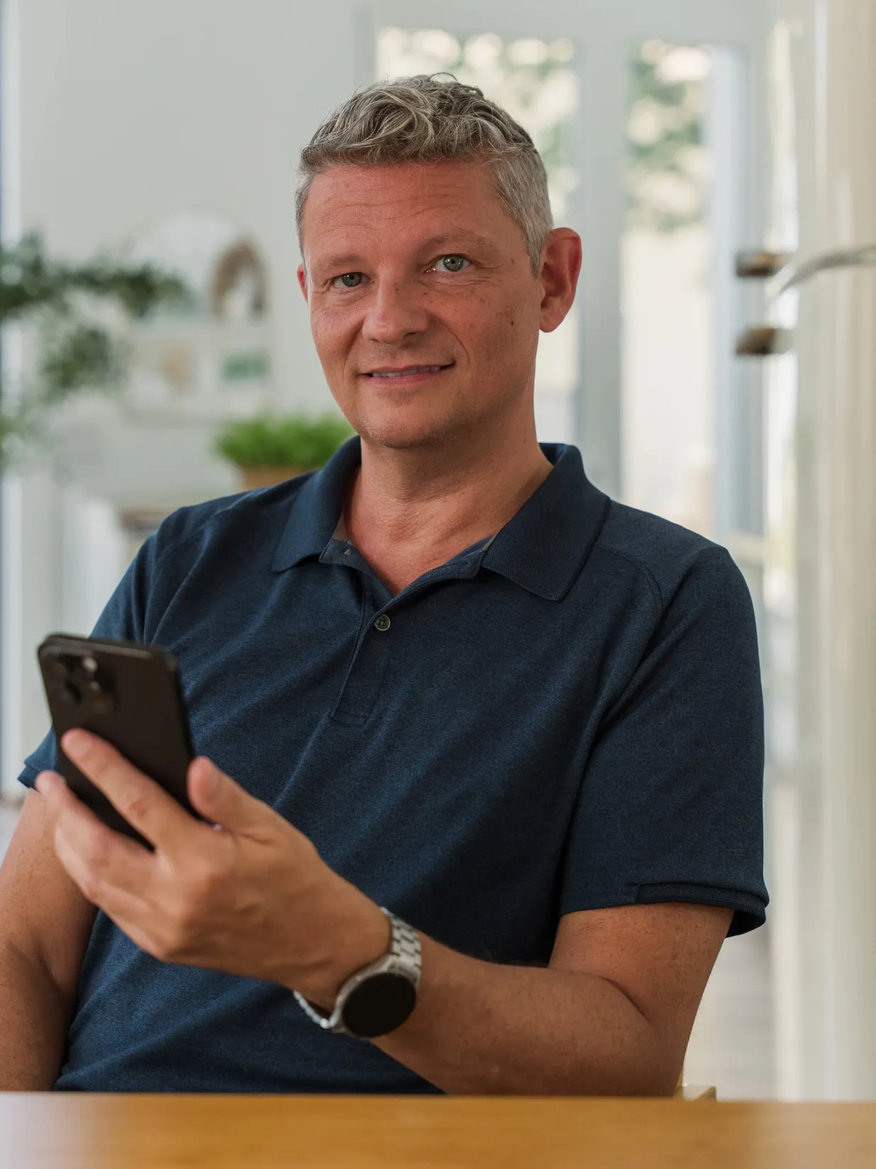 Andrew, UNA’s founder and developer, smiling at a table in a bright room, his iPhone in hand